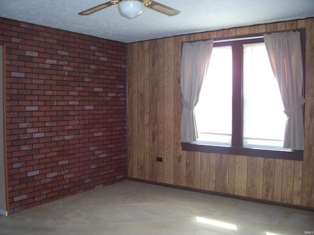 empty room with a textured ceiling, ceiling fan, brick wall, wood walls, and baseboards