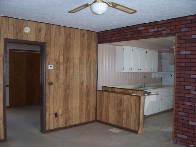 kitchen with wooden walls, ceiling fan, a textured ceiling, white cabinetry, and a sink