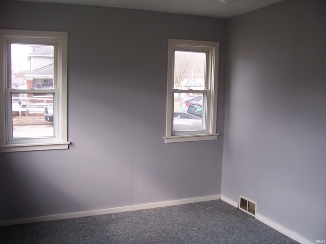 carpeted spare room featuring visible vents, baseboards, and a wealth of natural light