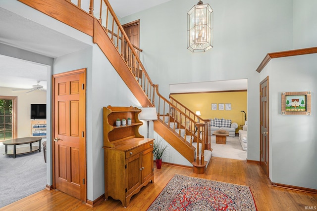 stairs with a towering ceiling, baseboards, a chandelier, and wood finished floors