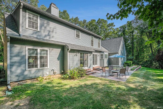 back of house with roof with shingles, a patio, a chimney, and a lawn