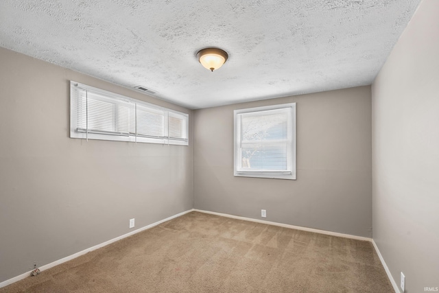 spare room featuring a textured ceiling, carpet flooring, visible vents, and baseboards