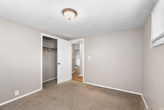 unfurnished bedroom with carpet, a closet, a textured ceiling, and baseboards