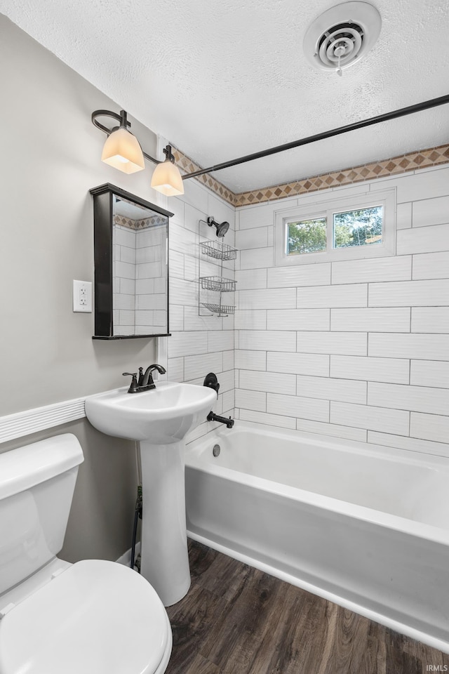 full bath featuring a textured ceiling, toilet, wood finished floors, visible vents, and tub / shower combination