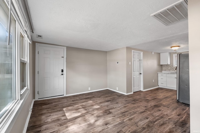 unfurnished living room featuring dark wood-style floors, baseboards, visible vents, and a textured ceiling