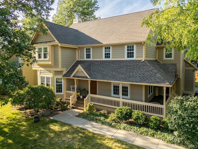 view of front facade with a shingled roof, a chimney, a front lawn, and a porch