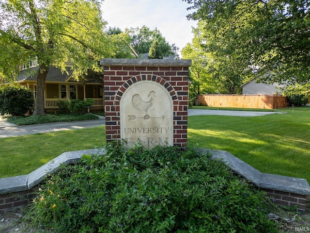 community / neighborhood sign featuring fence and a lawn