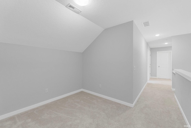 bonus room with a textured ceiling, light colored carpet, visible vents, baseboards, and vaulted ceiling