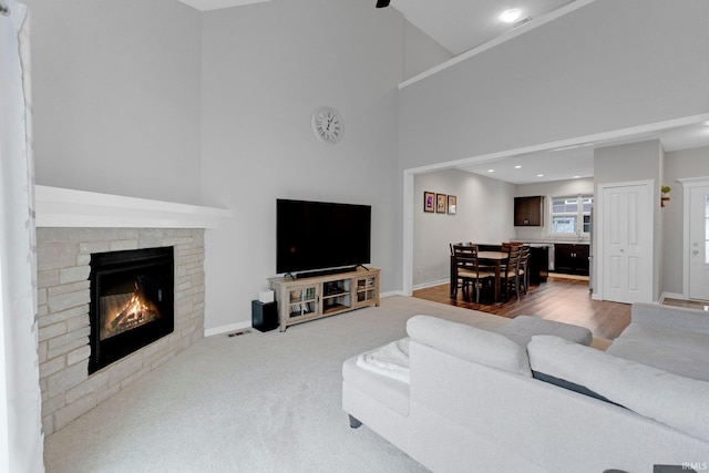 carpeted living area with a fireplace, a towering ceiling, baseboards, and wood finished floors