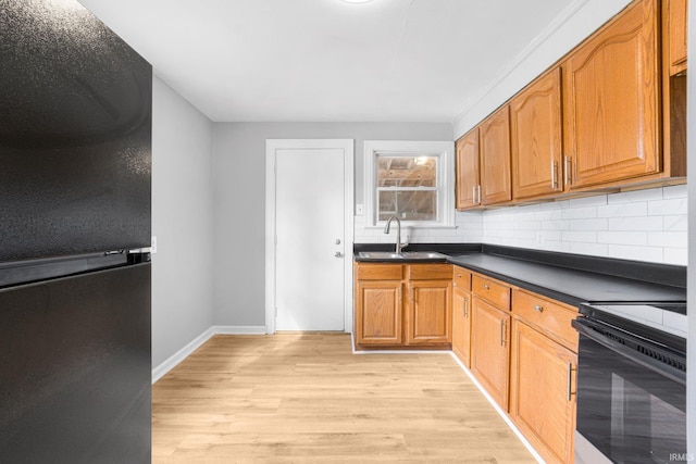 kitchen with range with electric cooktop, dark countertops, a sink, light wood-type flooring, and backsplash