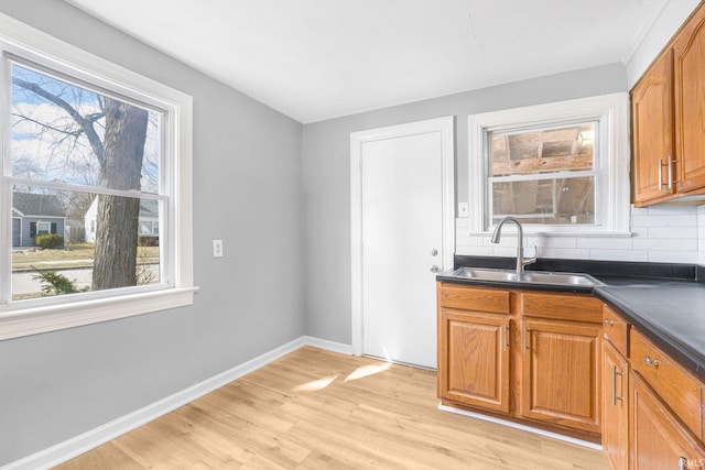 kitchen with tasteful backsplash, baseboards, dark countertops, light wood-type flooring, and a sink