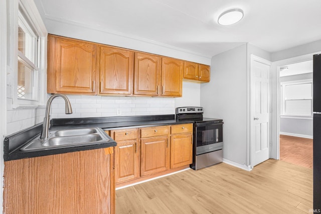 kitchen with light wood finished floors, decorative backsplash, dark countertops, stainless steel electric range oven, and a sink