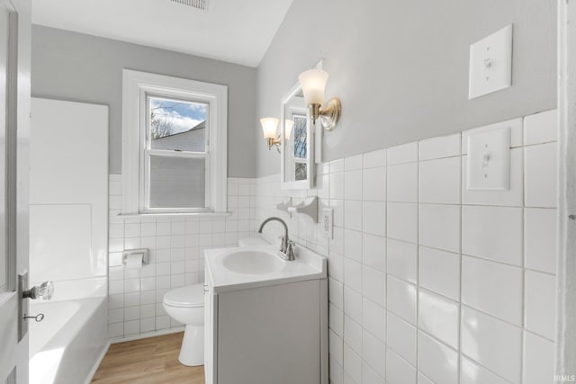 bathroom with tile walls, toilet, a bathing tub, vanity, and wood finished floors