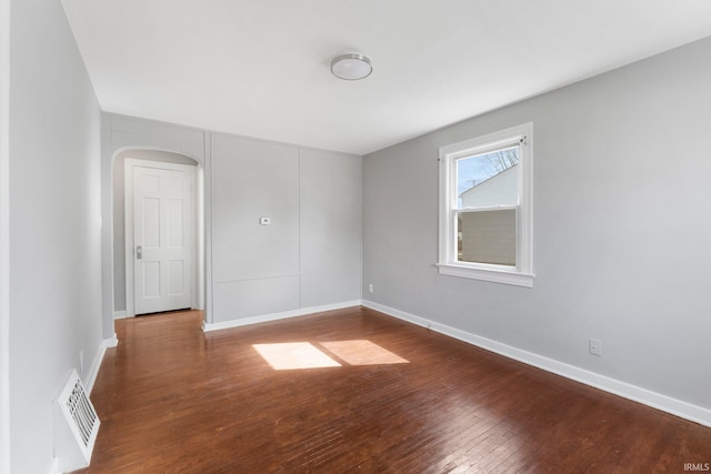 empty room with arched walkways, hardwood / wood-style floors, visible vents, and baseboards