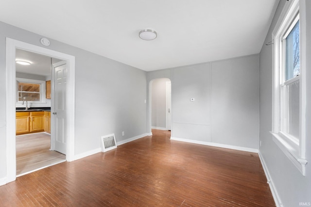 empty room featuring arched walkways, wood finished floors, a sink, visible vents, and baseboards