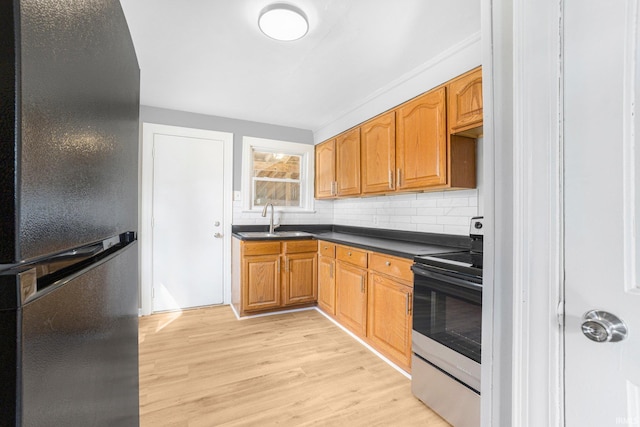 kitchen with electric range, a sink, freestanding refrigerator, light wood finished floors, and dark countertops