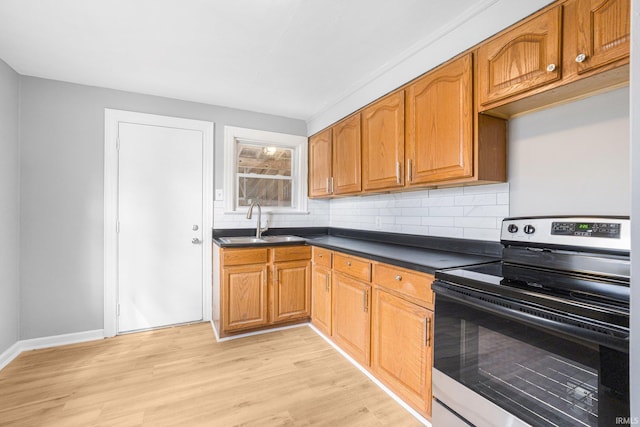 kitchen with light wood finished floors, electric range, decorative backsplash, dark countertops, and a sink