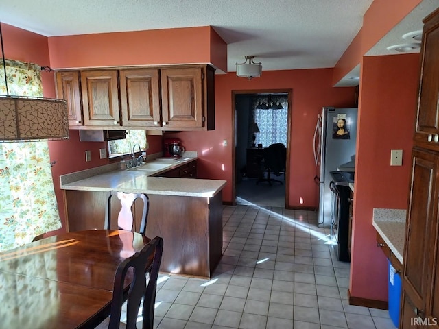 kitchen featuring light tile patterned floors, freestanding refrigerator, a peninsula, light countertops, and a sink