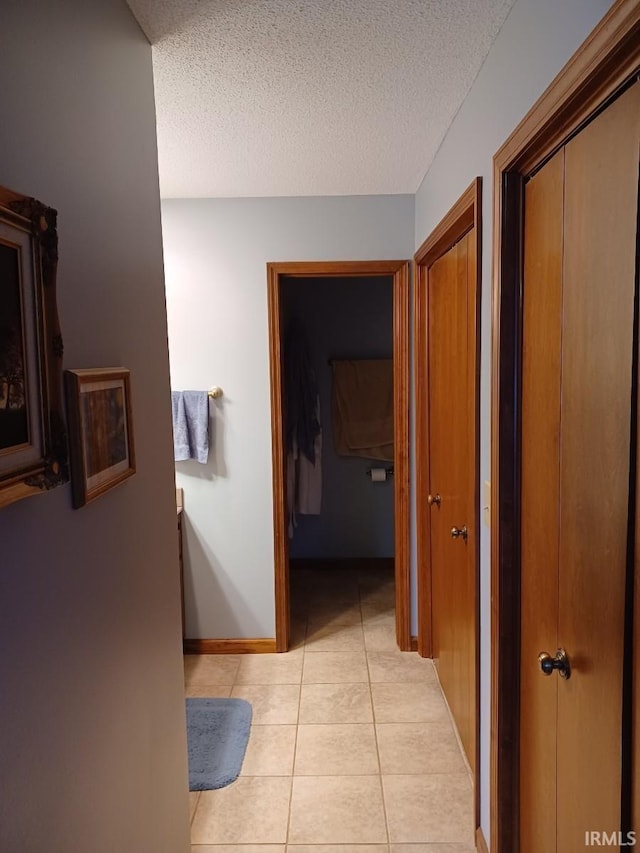 corridor with a textured ceiling, baseboards, and light tile patterned floors