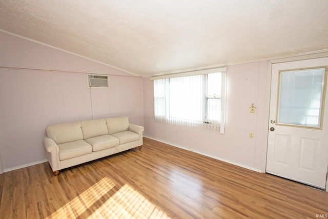 unfurnished living room featuring an AC wall unit, vaulted ceiling, a textured ceiling, and wood finished floors