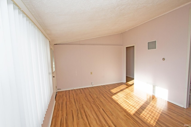 empty room featuring lofted ceiling, light wood-style floors, visible vents, and a textured ceiling