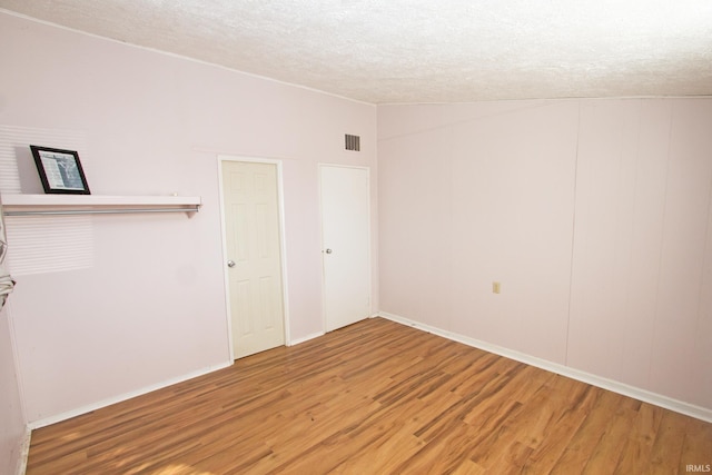 unfurnished room featuring lofted ceiling, light wood finished floors, visible vents, and a textured ceiling