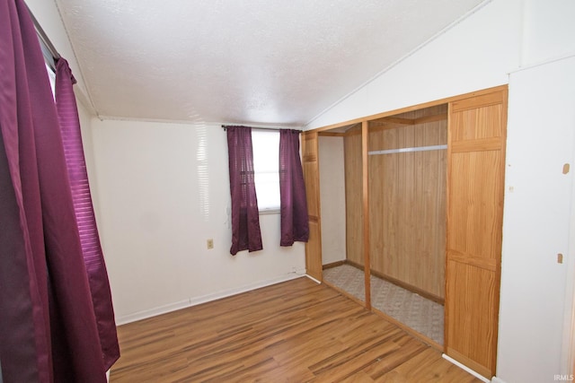 unfurnished bedroom featuring lofted ceiling, a textured ceiling, wood finished floors, baseboards, and a closet