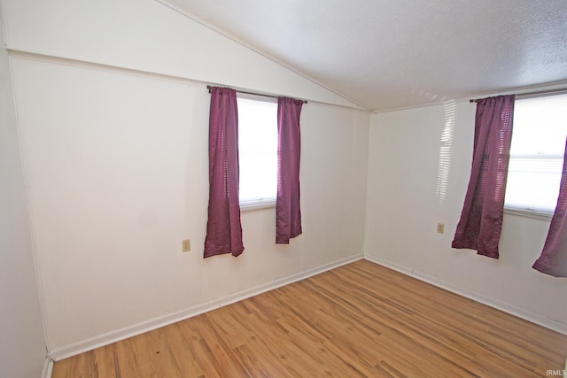 empty room featuring plenty of natural light, vaulted ceiling, a textured ceiling, and wood finished floors