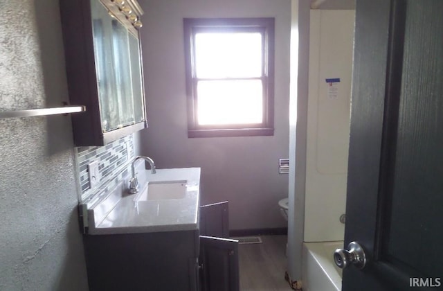 bathroom featuring a tub to relax in, vanity, toilet, and decorative backsplash