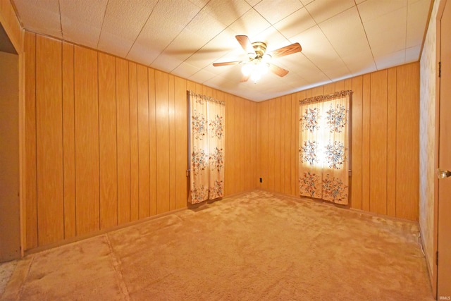 carpeted empty room featuring a ceiling fan and wooden walls