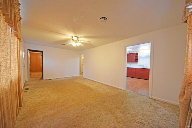 spare room featuring light carpet, ceiling fan, visible vents, and baseboards