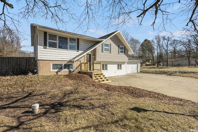 raised ranch featuring a garage, driveway, brick siding, and fence