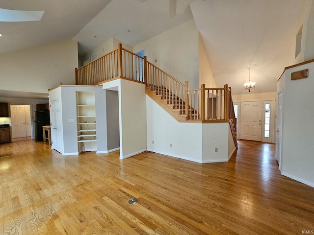 unfurnished living room featuring high vaulted ceiling, light wood-type flooring, an inviting chandelier, and stairs