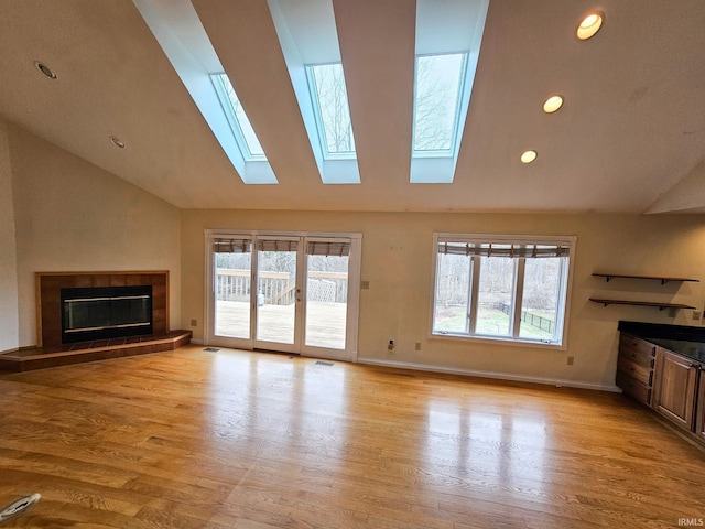 unfurnished living room featuring light wood-style flooring, a tiled fireplace, baseboards, and a wealth of natural light