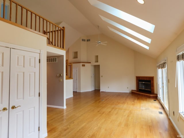 unfurnished living room with light wood-type flooring, a skylight, a glass covered fireplace, and visible vents