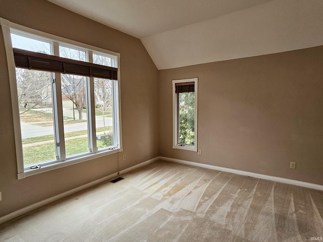 spare room featuring lofted ceiling, light colored carpet, visible vents, and baseboards