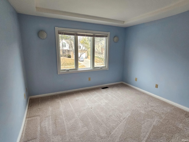 carpeted empty room featuring a tray ceiling, visible vents, and baseboards