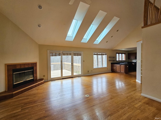 unfurnished living room with light wood-style floors, baseboards, high vaulted ceiling, and a tile fireplace