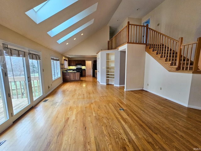 unfurnished living room with a skylight, visible vents, stairway, high vaulted ceiling, and light wood-type flooring