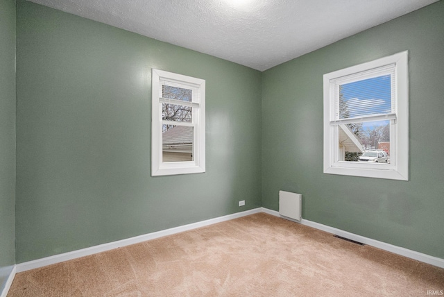 carpeted empty room with visible vents, a textured ceiling, and baseboards