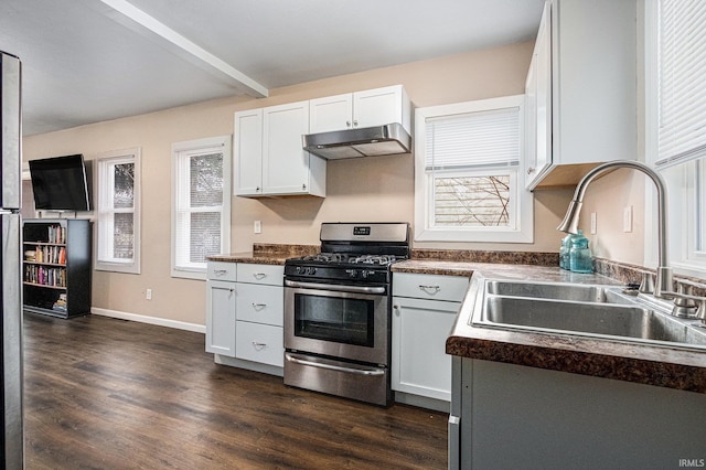 kitchen featuring dark countertops, dark wood-style floors, under cabinet range hood, stainless steel range with gas cooktop, and a sink