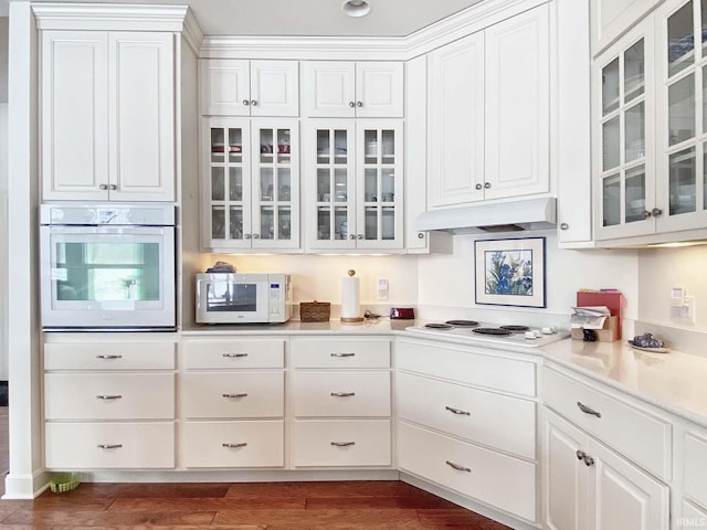 kitchen with dark wood-style flooring, glass insert cabinets, white cabinetry, white appliances, and under cabinet range hood