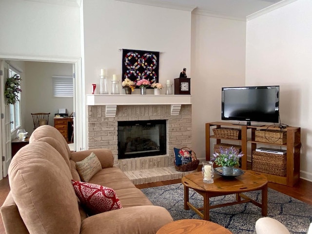 living room featuring a brick fireplace, crown molding, baseboards, and wood finished floors