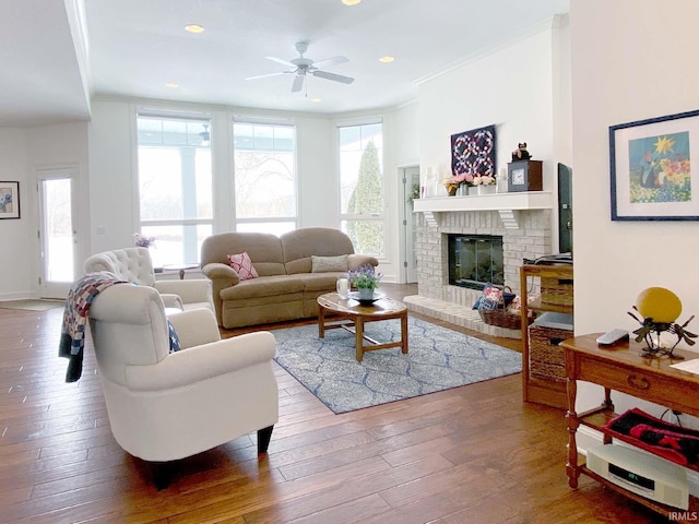 living room featuring recessed lighting, wood-type flooring, ornamental molding, a brick fireplace, and ceiling fan