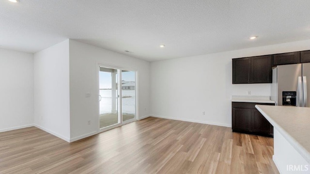 kitchen with a textured ceiling, baseboards, light countertops, light wood finished floors, and stainless steel fridge