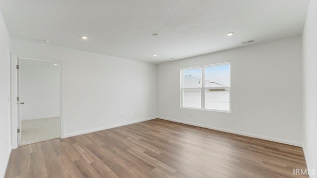 spare room featuring a textured ceiling, recessed lighting, wood finished floors, and baseboards