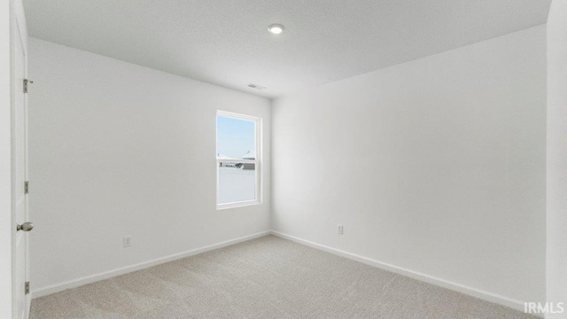 spare room featuring light carpet, visible vents, and baseboards