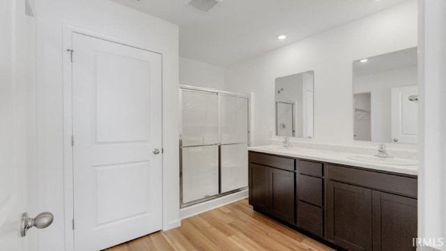 bathroom with wood finished floors, a sink, visible vents, double vanity, and a stall shower