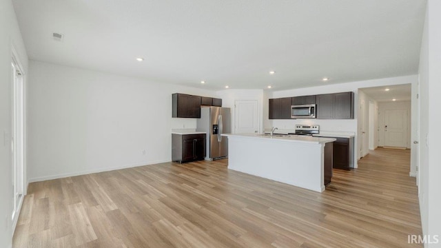 kitchen featuring stainless steel appliances, dark brown cabinets, light countertops, light wood-style floors, and a sink