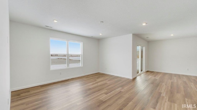 empty room with a textured ceiling, recessed lighting, visible vents, baseboards, and light wood-type flooring